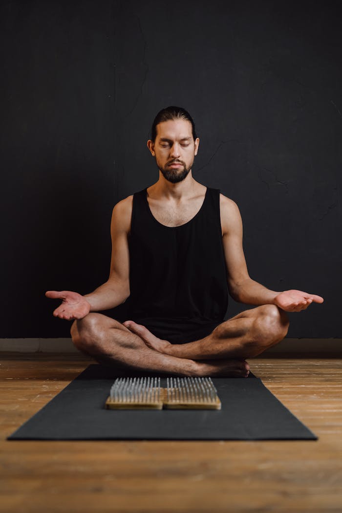 A man practicing meditation in a calm studio setting, seated on a yoga mat.